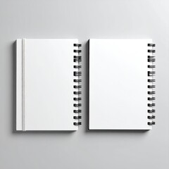 Two blank spiral-bound notebooks, side-by-side, on a light gray surface.  Both notebooks are white, featuring black spiral binding.  A white elastic band is visible on one