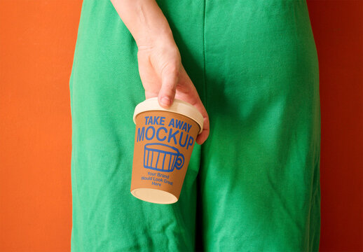 Woman in green shorts holds a takeaway glass behind their back against an orange wall. PSD mockup.