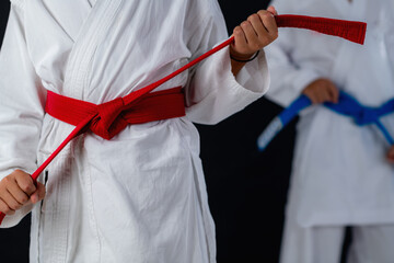 Detail from a karate training, with two boys in karate uniforms showing hand stance and belt knot against black background.