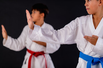 Boys in karate training executing focused karate kata routine against black background. Shows disciplined control, aligned movements, and traditional martial arts form.