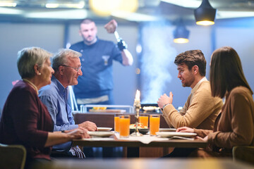 Family gathers for iftar to break fast during Ramadan in a restaurant setting with a chef preparing meals in the background