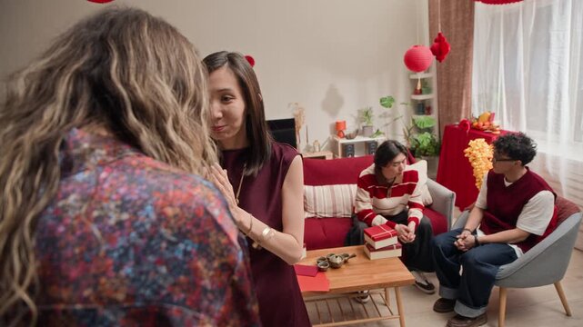 POV shot of four Asian friends celebrating Tet and sharing gifts in apartment decorated with traditional holiday elements