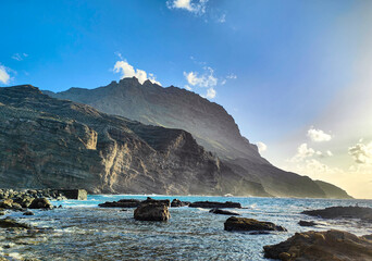 Dramatic volcanic cliffs at Playa de Alojera on the Atlantic coast at the sunset. Rugged rocky shoreline and ocean waves. Remote natural landscape with copy space. La Gomera, Canary Islands, Spain