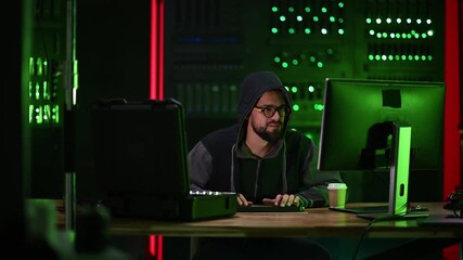 Hooded hacker typing on computer in server room at night - Powered by Adobe