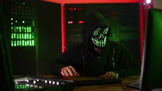Anonymous masked hacker typing in server room