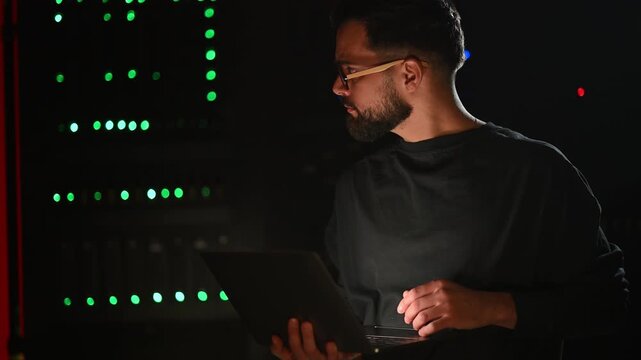 Male it administrator working on a laptop in a dark data center server room