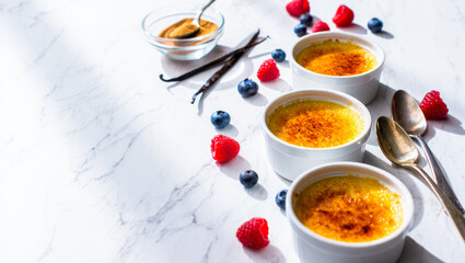 Delicious cr&egrave;me br&ucirc;l&eacute;e dessert with fresh berries and vanilla, gourmet presentation for culinary magazines or food blogs, elegant serving on white marble surface, copy space. Menu, recipe.