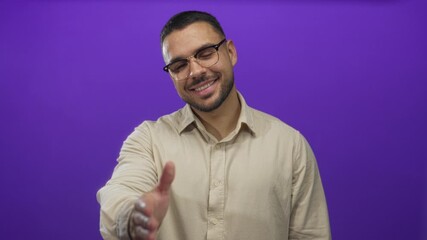 Man smiles and extends hand for a warm handshake in studio with vivid purple hue; greeting friendliness.