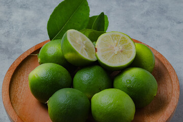 Fresh green limes arranged on a wooden plate with lime slices and leaves on a light background