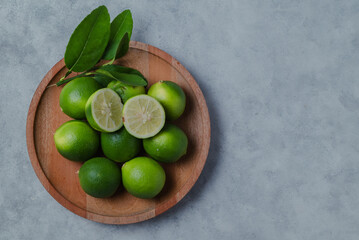 Fresh green limes arranged on a wooden plate with lime slices and leaves on a light background
