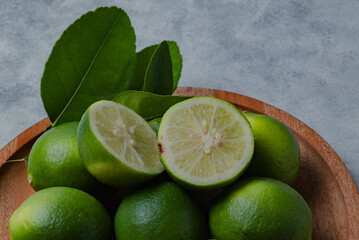 Fresh green limes arranged on a wooden plate with lime slices and leaves on a light background