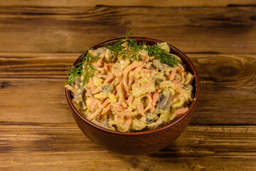 Salad with chicken breast, marinated mushrooms, carrot, eggs, boiled potato and mayonnaise on a wooden table