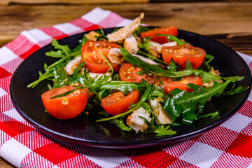 Roasted chicken breasts and salad with arugula and cherry tomatoes in a black plate