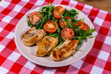 Roasted chicken breasts and salad with arugula and cherry tomatoes in a ceramic plate