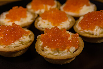 Tartlets with red caviar on a black plate. Festive food
