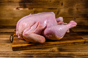Wooden cutting board with the whole uncooked chicken