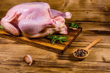 Wooden cutting board with the whole uncooked chicken, garlic and spices