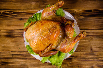 Plate with roasted whole chicken and lettuce leaves on a wooden table. Top view