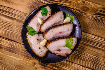 Slices of baked pork belly, garlic and parsley on a black plate. Top view
