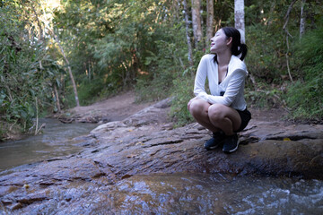 A woman is sitting on a rock by a river, looking at the water. Walking Trail Hiking forest concept.