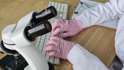 Laboratory worker types on keyboard while using microscope in research study