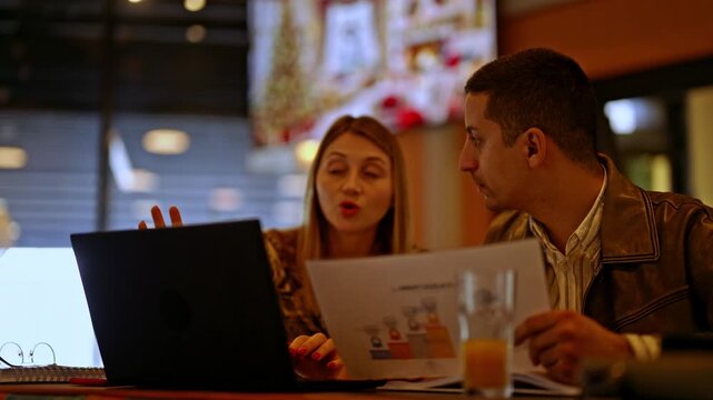 Two dedicated professionals engaged in a productive business meeting, analyzing charts and documents on a laptop while discussing future strategies and collaborating effectively.