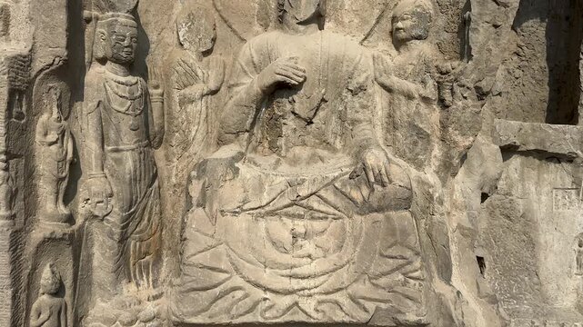 Damaged Buddhist sculpture of Buddha, disciples and bodhisattvas on cliff  of west hill at Longmen Grottoes, Luoyang, Henan, China. UNESCO World Heritage site. 