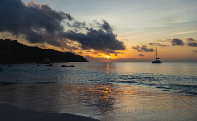 Golden hour sunset over a tranquil sea, with a lone sailboat on the horizon