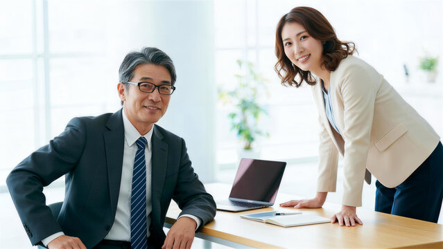 デスクで自信溢れる笑顔を見せるベテラン男性と若い女性の社員ペア
