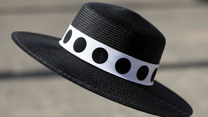 Stylish black hat with white polka dot band floating in air