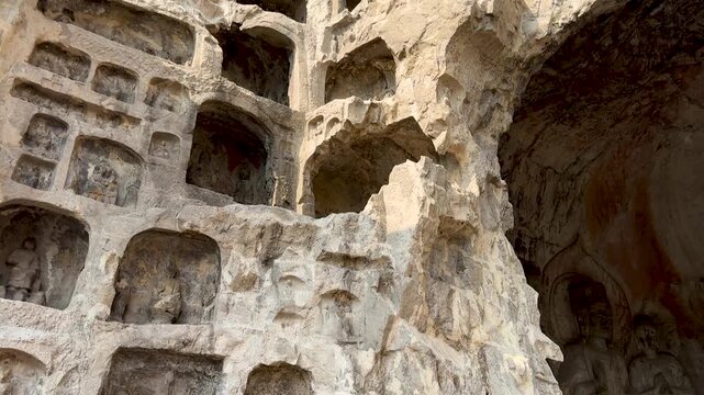 Small niches and caves on left side cliff of entrance to South Binyang Cave at Longmen Grottoes, Luoyang, Henan, China. UNESCO World Heritage site. Tourist attraction. 