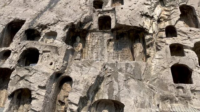 Small caves, niches and reliefs on cliff of west hill at Longmen Grottoes, Luoyang, Henan, China. UNESCO World Heritage site. Tourist attraction. 