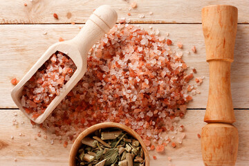 Himalayan salt placed in a wooden spoon and a container with dried herbs on a light-colored wooden surface