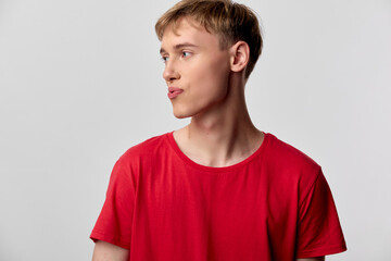 Young man in a red t shirt looks to the side in a studio setting with a neutral background, conveying casual fashion and a thoughtful, calm expression