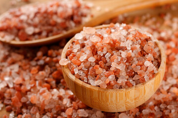 Granulated Himalayan salt in a wooden bowl on a light-colored wooden surface.