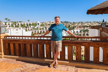 Confident Adult Man in Blue Shirt Standing the Terrace of an Egyptian Resort, Enjoying the Scenic View and Relaxing Atmosphere.