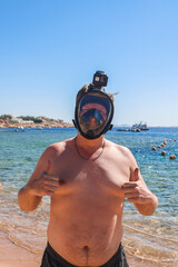 man wearing snorkeling mask stands on the beach of an Egyptian hotel ready to swim.