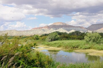 Landscape photograph showing a small lake and forest vegetation in front of layered colorful mountains at Nallıhan Kuş Cenneti, a protected natural area in Turkey.