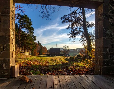 Rustic stone doorway frames a vibrant autumn landscape with rolling hills and wispy clouds on a sunny day