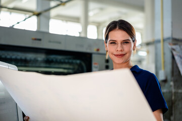 
A smiling female printing professional inspecting packaging printing in a modern print shop factory. Quality control, industrial manufacturing, and professional offset printing concept.