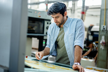 Professional worker inspecting printed materials in modern factory, checking quality and accuracy on production line. Concept of manufacturing process, quality control, and precision work.