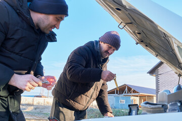Father and adult son checking oil level in car engine with open hood