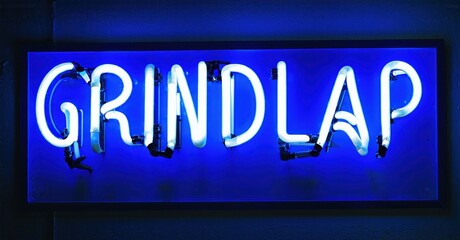Obraz premium Bright blue neon sign spells GRINDLAP. Rectangular frame surrounds glowing text against dark background. Simple, modern aesthetic.