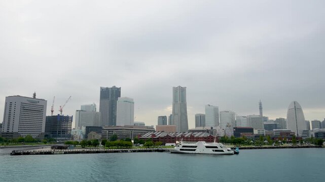 Viewed from a cruise ship. Features calm waters with boats, historic red brick warehouses, green parks, and the iconic Minato Mirai skyline with skyscrapers and Ferris wheel. Yokohama Port, Japan.