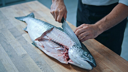 Chef filleting salmon fish on wooden cutting board in kitchen