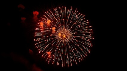 Beautiful single orange and red firework burst exploding in a spherical shape against a dark sky