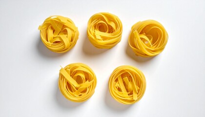 Four nests of uncooked tagliatelle pasta made of flat yellow ribbons coiled into circular shapes on white background.