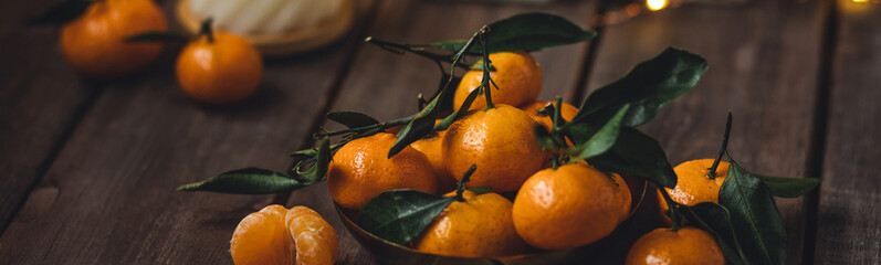 Atmospheric festive holiday composition with fresh orange tangerines, scented candle. Christmas decor, fairy lights, bokeh lights. New year spirit at home. Banner