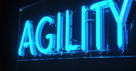 Bright blue neon sign spells agility. Dark background emphasizes glowing text. Modern aesthetic, simple design. Business concept, positive message.