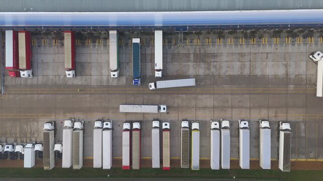 Top down aerial view of heavy semi trucks and trailers parked in loading bays at large distribution centre. Transport and logistics hub for import export in Milton Keynes, United Kingdom. 